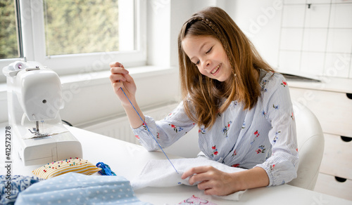 pretty and young schoolgirl is sitting by the table in her parents office embroidering, doing needlework, stitching photo