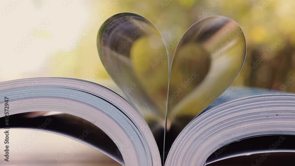 close-up of heart shape from book for love on wood table with blurred nature background in wind blowing with sunlight shining, zoom out shots
