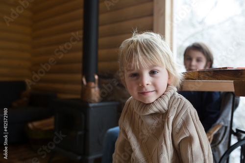 Cute toddler child in a little fancy wooden cottage, reading a book, drinking tea