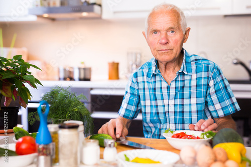 senor man preparing fresh vegetable salad at home in the kitchen