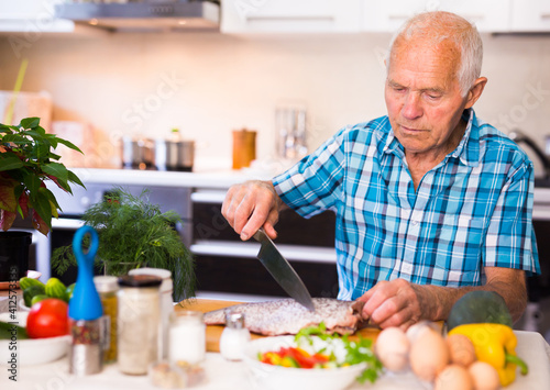 elderly man preparing fish at home in the kitchen