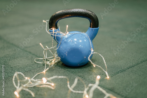 Fototapeta Naklejka Na Ścianę i Meble -  Kettle bells in a Gym. Christmas fitness composition with blue dumbbells, gift on white background with bokeh and show. Greeting card for fitness club with copy space.