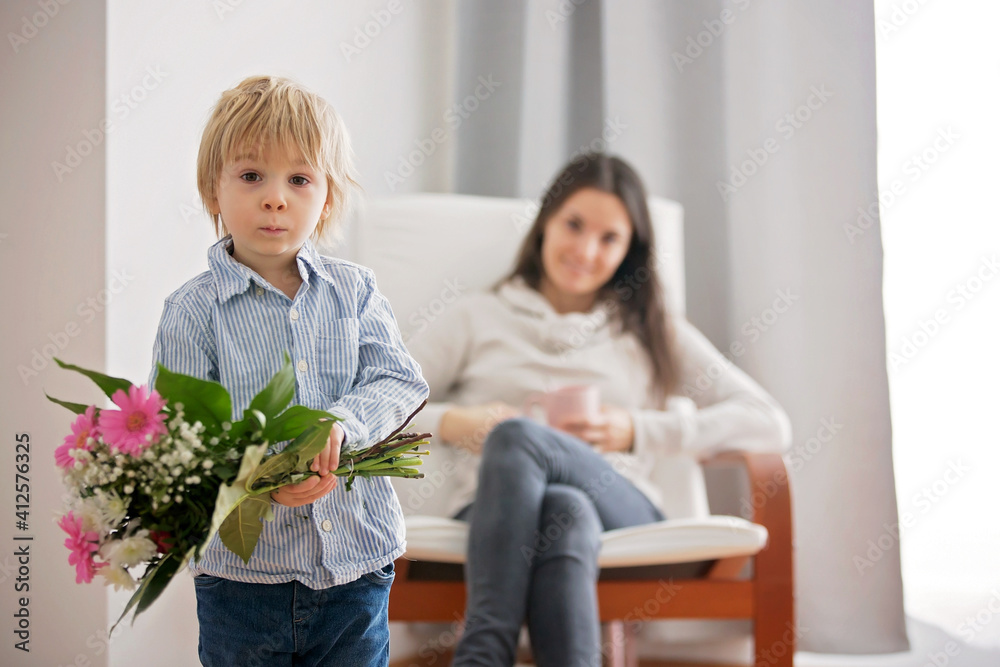 Beautiful blond boy, giving mother flowers and box with little gift for mothers day Beautiful blond boy, giving mother flowers and box with little gift for mothers day