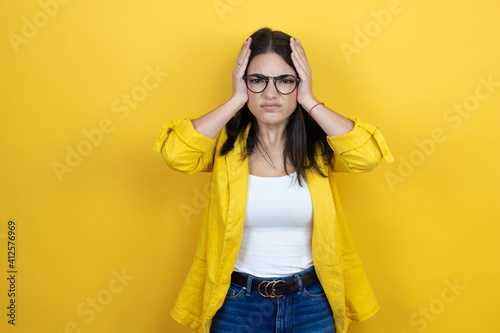 Young brunette businesswoman wearing yellow blazer over yellow background thinking looking tired and bored with hands on head