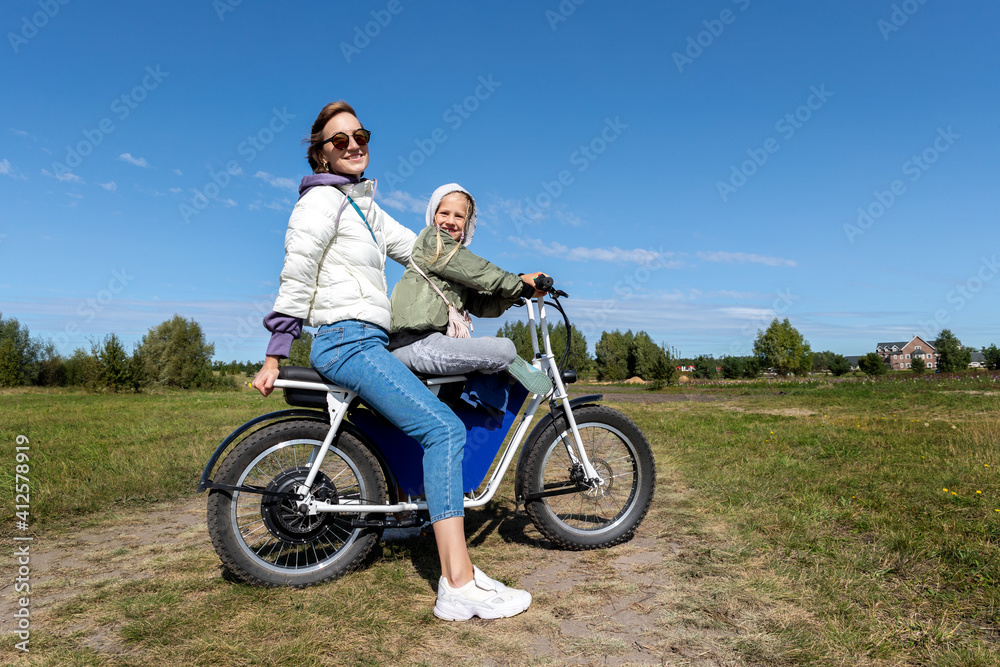 Young adult beautiful mother and daughter enjoy having fun riding electric scooter bike or rural countryside dirt road on bright sunny day. Mom with child road trip nature adventure travel