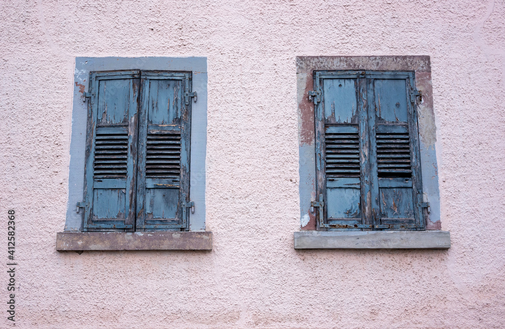 Facade of an old abandoned building with peeling light blue paint on window shades.