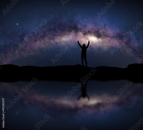 Female silhouette raises arms in front of a bright Milky Way night sky. Concept about open air sport activity, adventure, travel.