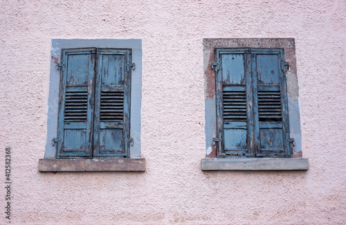 Facade of an old abandoned building with peeling light blue paint on window shades.