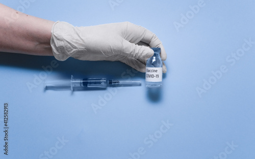 Syringe and vaccine vial glass bottle for vaccination against COVID-19 SARS-CoV-2 coronavirus pandemic in hand with medical glove. Vaccination concept. Top view, flat lay, copy space. 