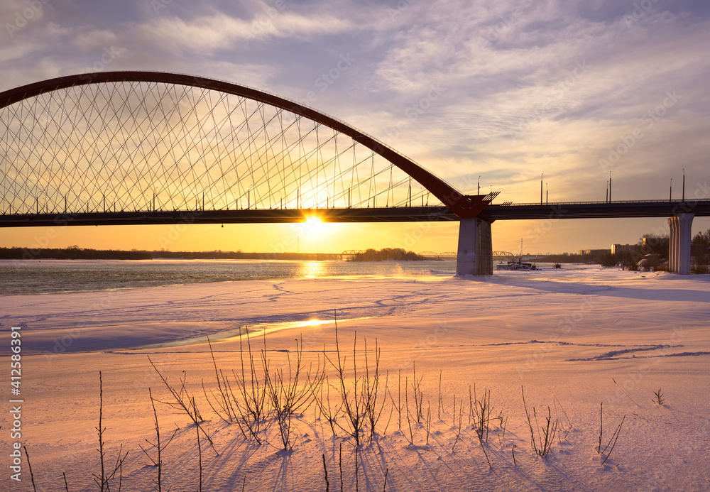 Naklejka premium Winter morning on the Ob. Bright sunrise under the arch of the Bugrinsky automobile bridge on the frozen river bank in Novosibirsk