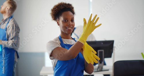 Portrait of african female janitor putting on gloves working in office photo