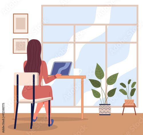 Office woman at a desk with a laptop back view. Business woman or a clerk working at her office table near big window. Freelancer at home office. Manager, enterpreneur performs work on a computer
