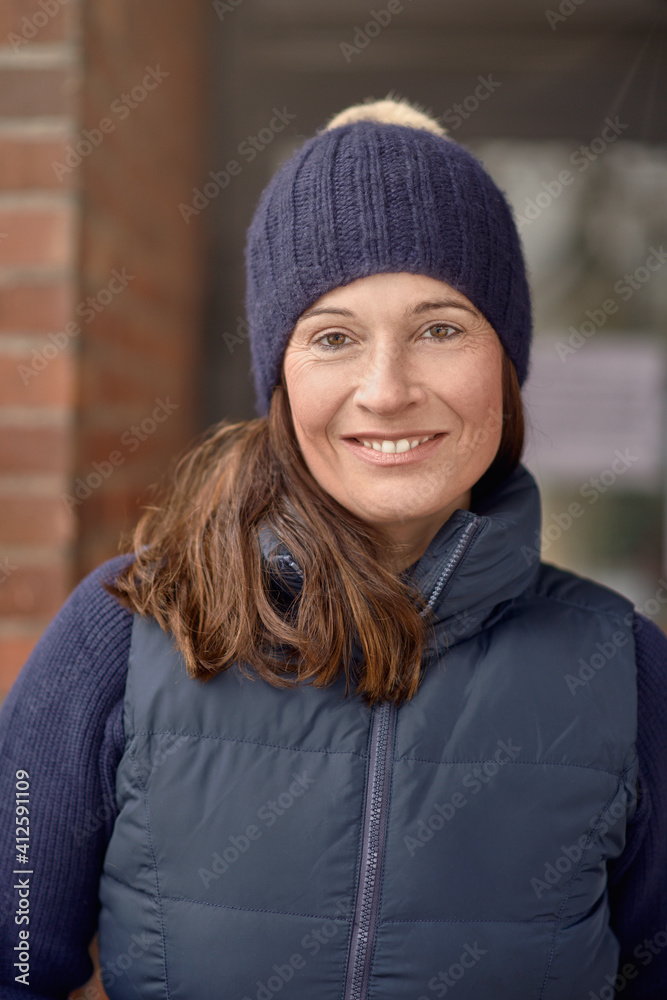 Attractive friendly smiling woman in blue winter outfit with knitted beanie hat and warm jacket in a close up head and shoulders outdoor portrait Attractive friendly smiling woman in blue winter outfit with knitted beanie hat and warm jacket in a close up head and shoulders outdoor portrait