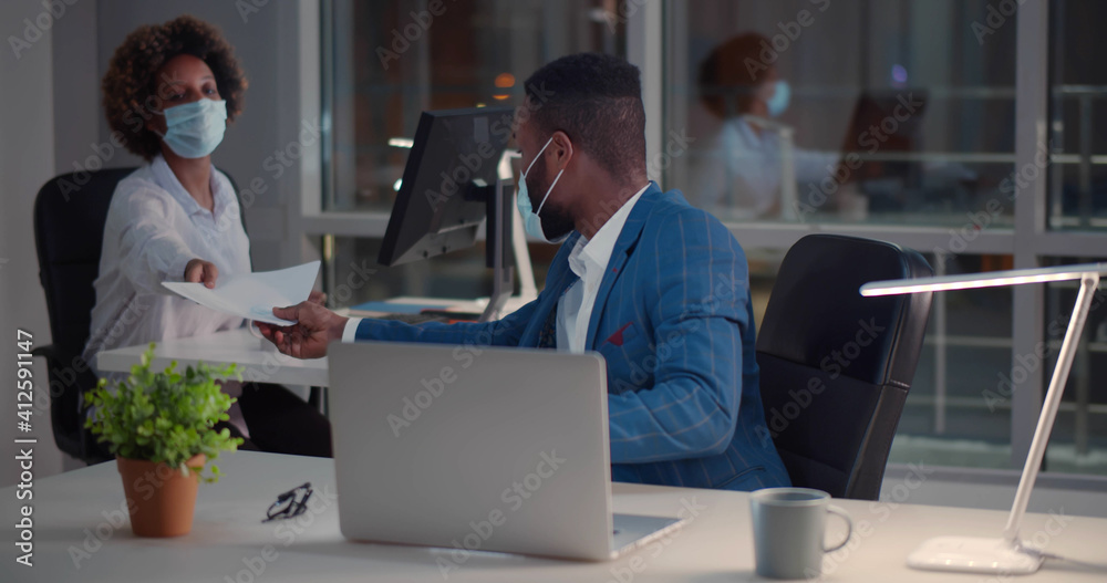 Afro-american businessman and businesswoman wearing face masks working in office
