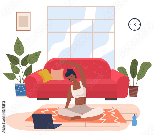 Woman doing yoga exercise, is engaged in a video lesson with a laptop. Young dark skinned fit girl sitting in lotus position at home. Female is taking care of her health, leads a healthy lifestyle
