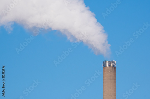 A closeup of an industrial smoke pipe against clear blue sky.