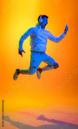 Flying. Caucasian man's portrait isolated on yellow studio background in mixed neon light. Listening music in headphones. Concept of human emotions, facial expression, sales, ad, fashion. Copyspace. © master1305