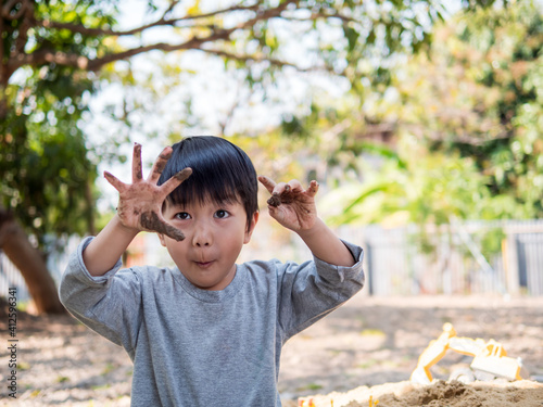 Asian cute child boy showing dirty black hands with clay, soil with wow funny face while playing outdoor. Happy kid enjoy in relaxing day, preschool learning and freedom concept.