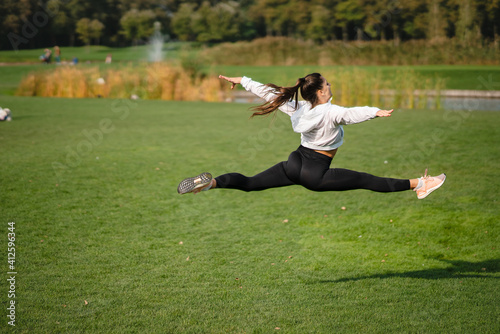Sport girl jumping in the air on nature demonstrate perfect stretching.