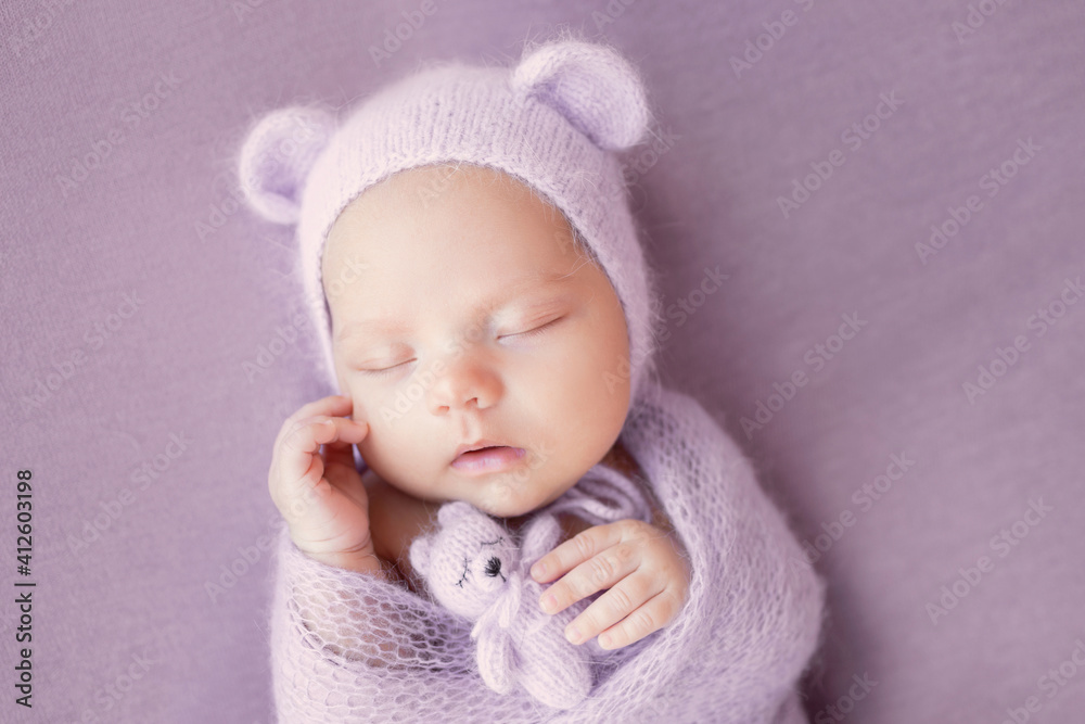 Newborn baby girl on a gray background in a hat with ears. A sweet newborn baby is sleeping. The first photo session of the baby.