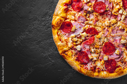 Pizza with Mozzarella cheese, salami, chicken meat, bacon, ham, Tomato sauce, pepper, spices. Italian pizza on Dark grey black slate background
