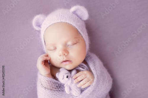 Newborn baby girl on a gray background in a hat with ears. A sweet newborn baby is sleeping. The first photo session of the baby.