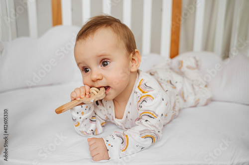 Fotografie Baby girl chewing wooden teething toy lying  in cradle in baby's room