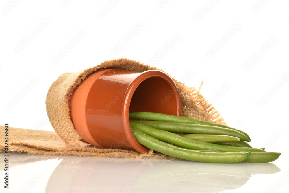 A few pods of bright green, organic, natural, ripe beans with a clay glass and a jute napkin, on a white background.