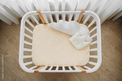 White wooden baby crib with pillows shaped clouds and crown in baby's room. Top view of child's bed photo