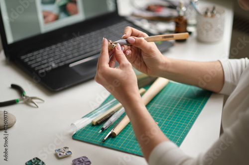 woman jeweler conducts online lesson in front of laptop. the teacher is taking online classes or watching a video tutorial on creating jewelry photo