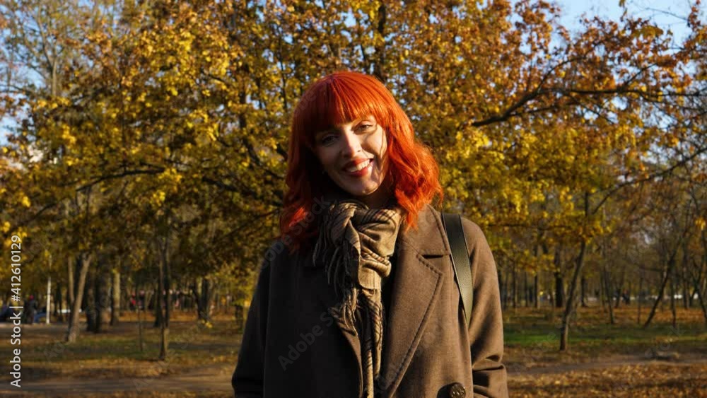 portrait of a girl with red hair on a background of autumn foliage from a tree, looks at the camera and smiles, in bright sunlight from the sun portrait of a girl with red hair on a background of autumn foliage from a tree, looks at the camera and smiles, in bright sunlight from the sun
