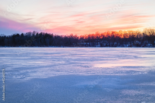 Snow covered lake reflecting colors of sunset in winter