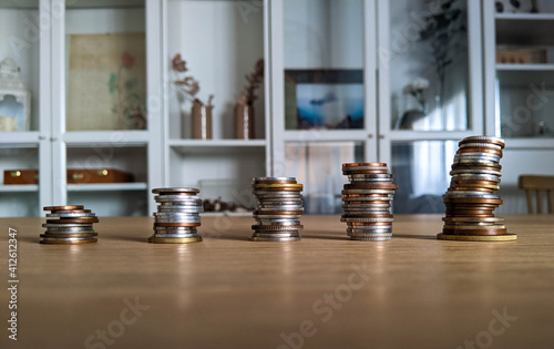 Save money concept. Stack of coins at home on a wooden table and a bookshelf in the background