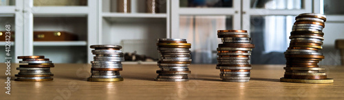 Save money concept. Stack of coins at home on a wooden table and a bookshelf in the background