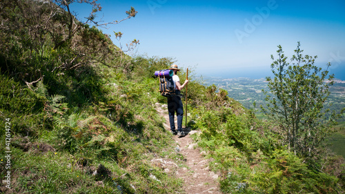 Caminante de peregrino con mochila, sombrero de paja y palo de madera por camino entre montañas en Asturias photo