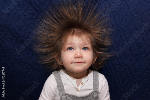 Portrait of a little smiling girl with electrified hair on a blue background.
Electricity power concept.