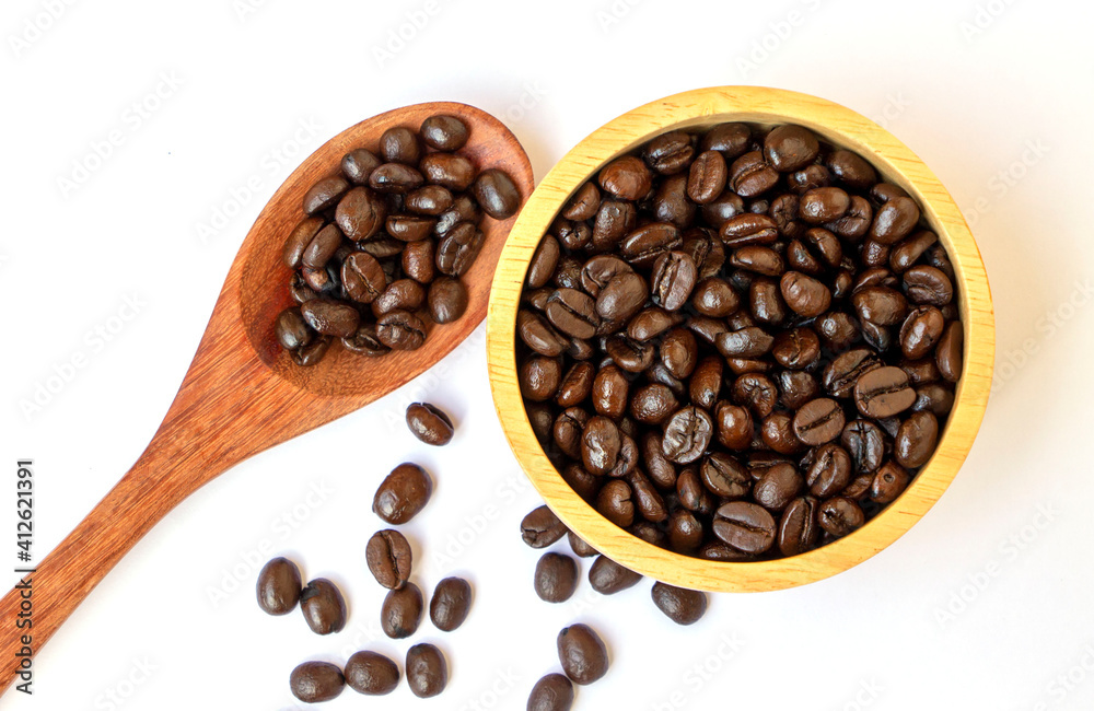 Obraz premium organic brown roasted arabica coffee beans in a wooden bowl and spoon on white background. Focus on coffee beans in a bowl. Famous and good quality coffee bean from Chiangmai, Thailand