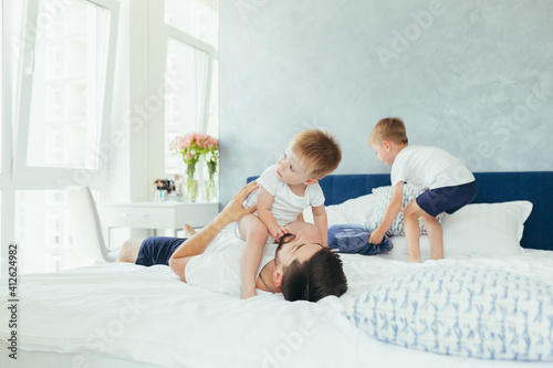 husband father playing with his children, two little boys brothers, in a large bedroom