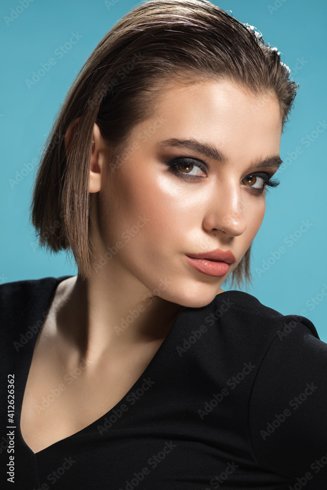 Naklejka premium Magazine style. Portrait of young female fashion model isolated on blue studio background. Beautiful caucasian woman with trendy make-up and well-kept skin. Style and beauty concept. Close up.
