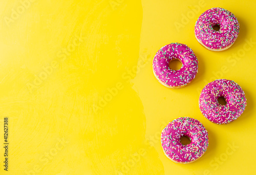 Pink glaze donuts with colorful sprinkles on yellow background. Minimalist concept. Top view.