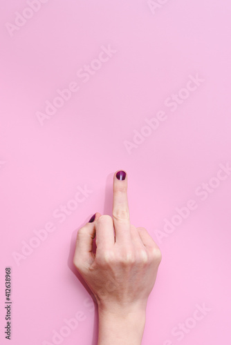 hand of a caucasian female raising middle finder showing an offensive gesture on a pink background
