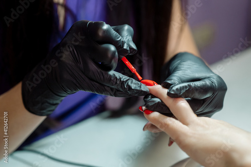 Manicurist in protective gloves applies nail polish to a woman's nails in a beauty salon. Professional manicure in a nail studio, photo of the process 