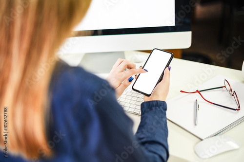 cropped shot of a young woman working from home using smart phone and computer, woman's hands using smart phone in interior, woman at home workplace using technology,