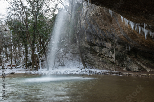 Waterfall in the winter forest. Beautiful view of the falling purest mountain river. A cliff face with icicles hanging down. Snow-covered trees, fresh air, day trips. Kozyrek waterfall in the Crimea.