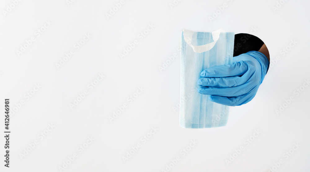 Coronavirus prevention medical masks in protective blue gloves in hand through grey paper hole. Vaccination shots to prevent infectious diseases. Coronavirus prevention medical masks in protective blue gloves in hand through grey paper hole. Vaccination shots to prevent infectious diseases.