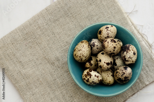 Quail eggs in a turquoise bowl, on a beige napkin and white backdrop. 