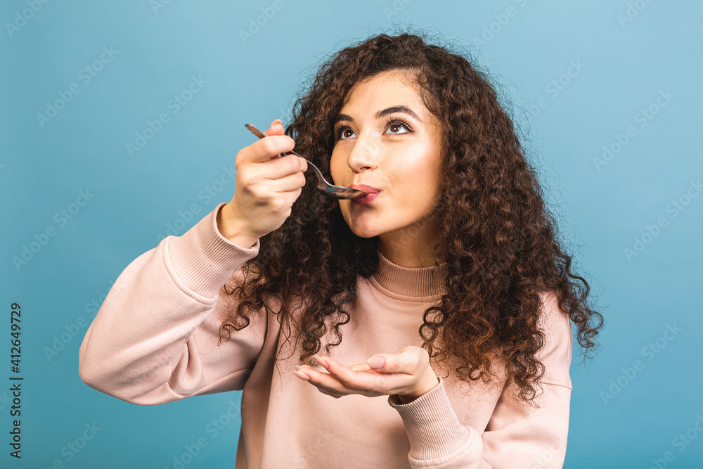 Photo of beautiful curly lady holding metal spoon in mouth look up empty space dreaming about tasty food isolated blue background.