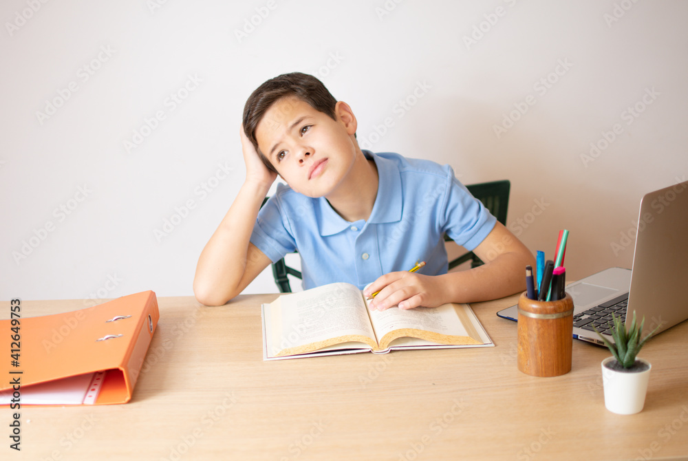 A young boy learning over his homework reading his workbook. A young boy learning over his homework reading his workbook.