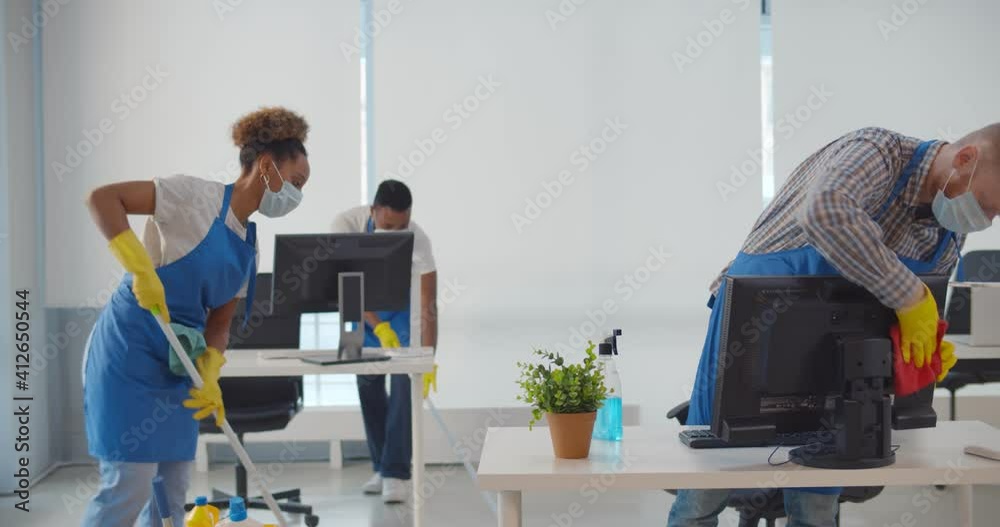 Team of diverse young cleaning service professionals in safety mask at work in office