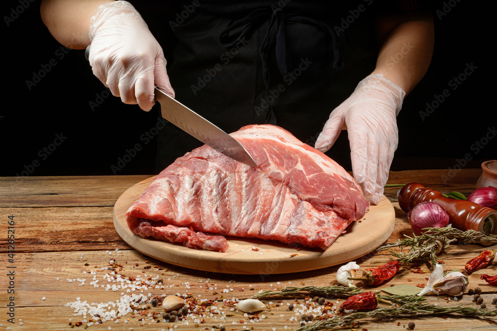 The chef uses his hands to slice pork ribs with a knife on a wooden cutting table. Selective focus. The concept of the cooking process.